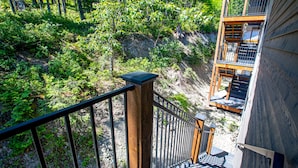 Eine Holztreppe führt zu einem Balkon mit Blick auf einen bewaldeten Hügel.