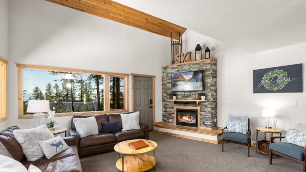 Ein gemütliches Wohnzimmer mit Kamin aus Stein, Ledersofas und einem großen Fenster mit Blick auf einen Wald.