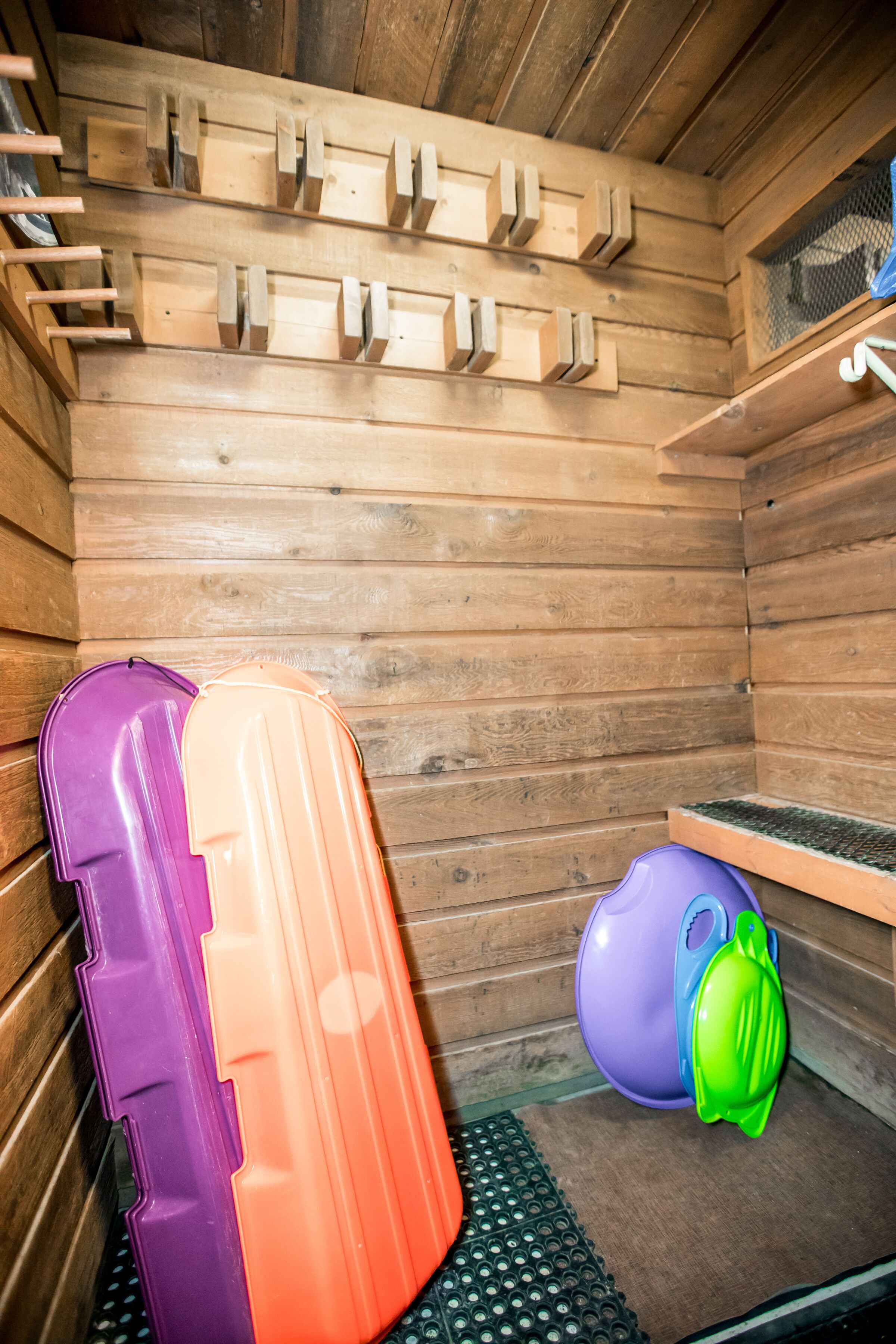 A wooden cabin interior with a sleeping area, a purple and orange inflatable mattress, and a green and purple inflatable pool.
