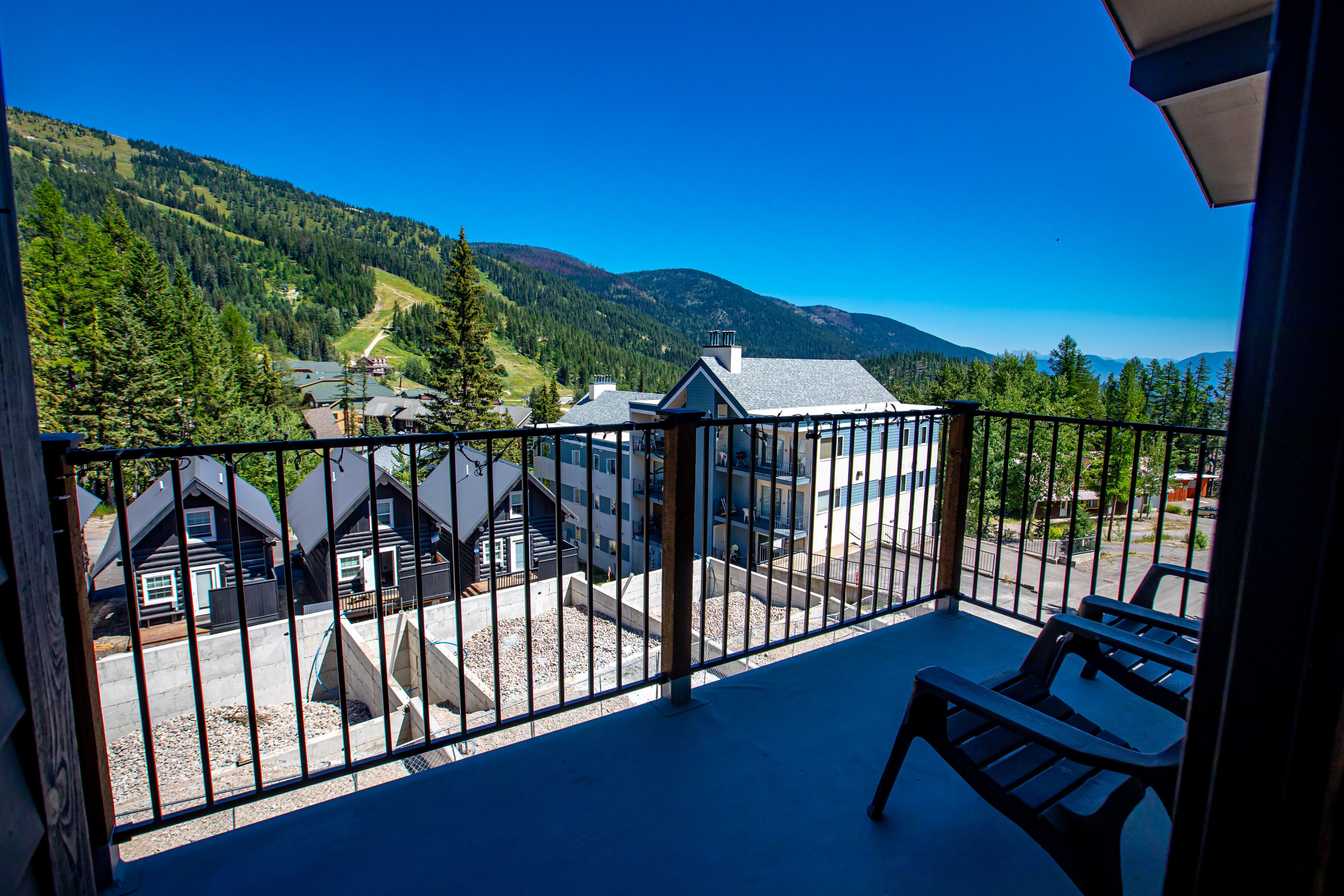 A balcony with a view of a mountain landscape, a pool area, and several buildings.