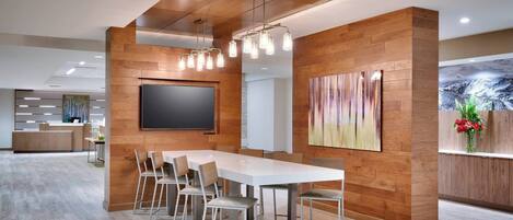 A modern conference room with a long table, chairs, a flat-screen TV, wooden panel walls, and a ceiling with exposed beams.