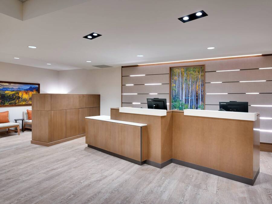 A reception area with a wooden reception desk, a painting on the wall, and a seating area with chairs and a sofa.