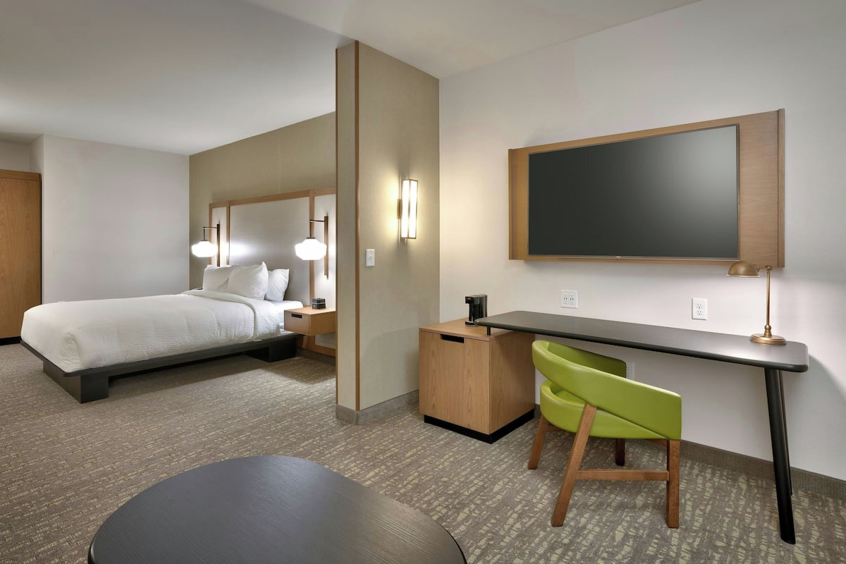 A hotel room with a bed, desk, chair, and a large mirror.