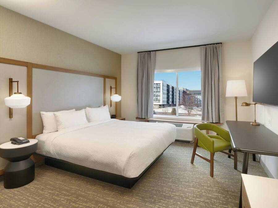 Une chambre d’hôtel avec un grand lit, un bureau, une chaise, une télévision et une fenêtre donnant sur la ville.