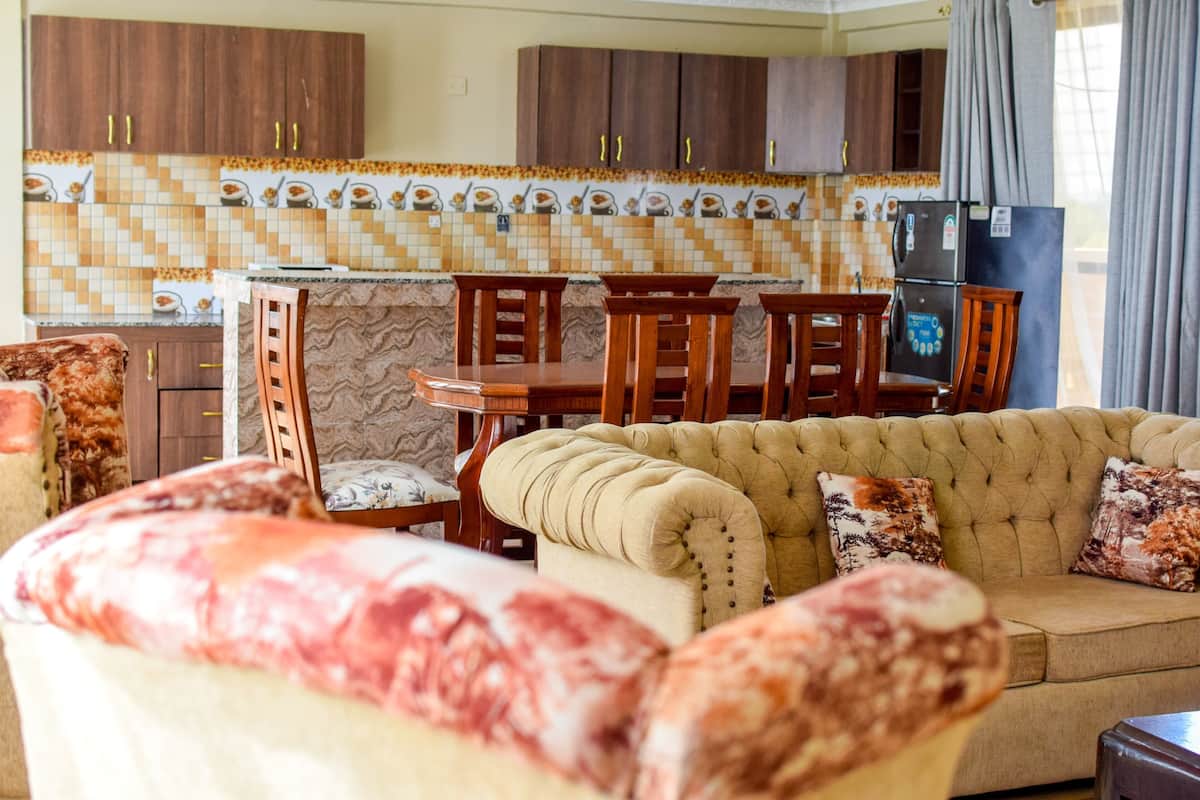 Un salon avec un canapé beige et des chaises en bois, une table à manger avec des chaises, et une cuisine avec des meubles en bois et un dosseret carrelé.