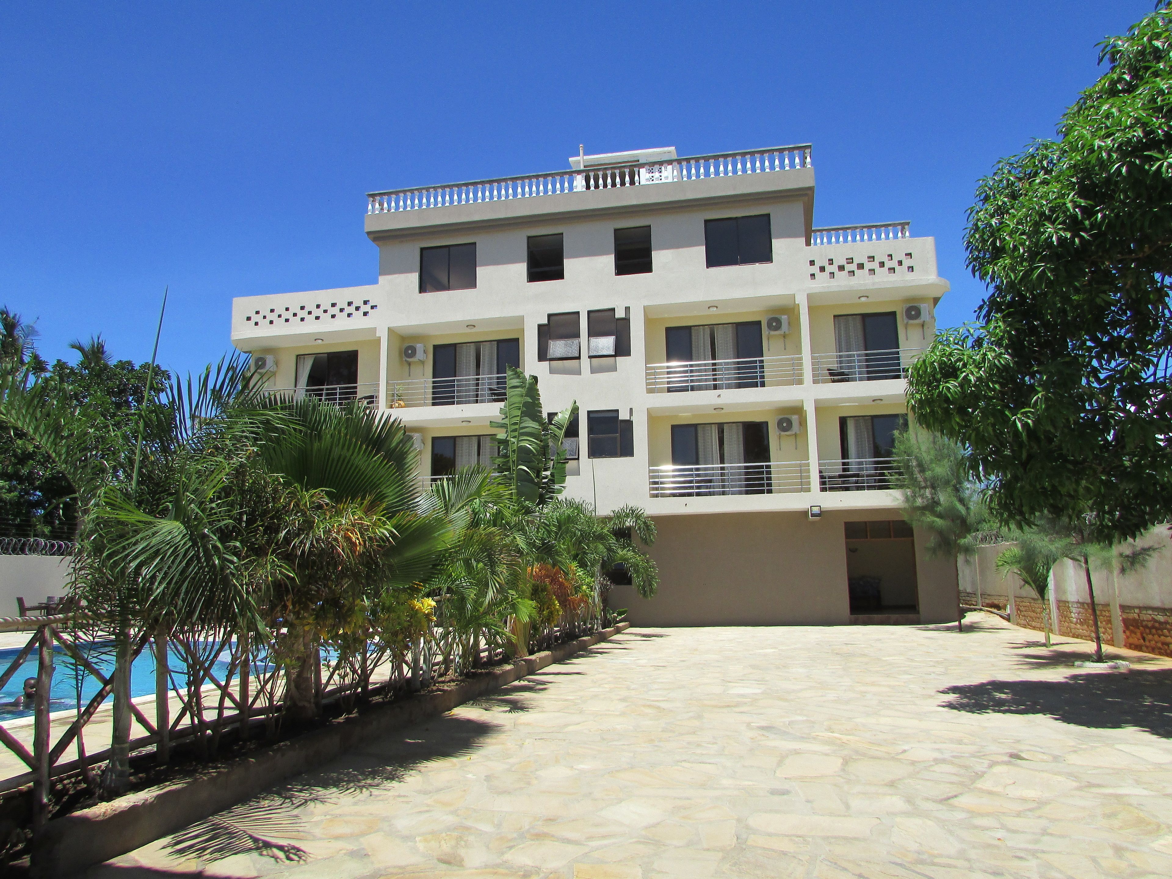 A multi-story building with balconies, a pool, and surrounding greenery.