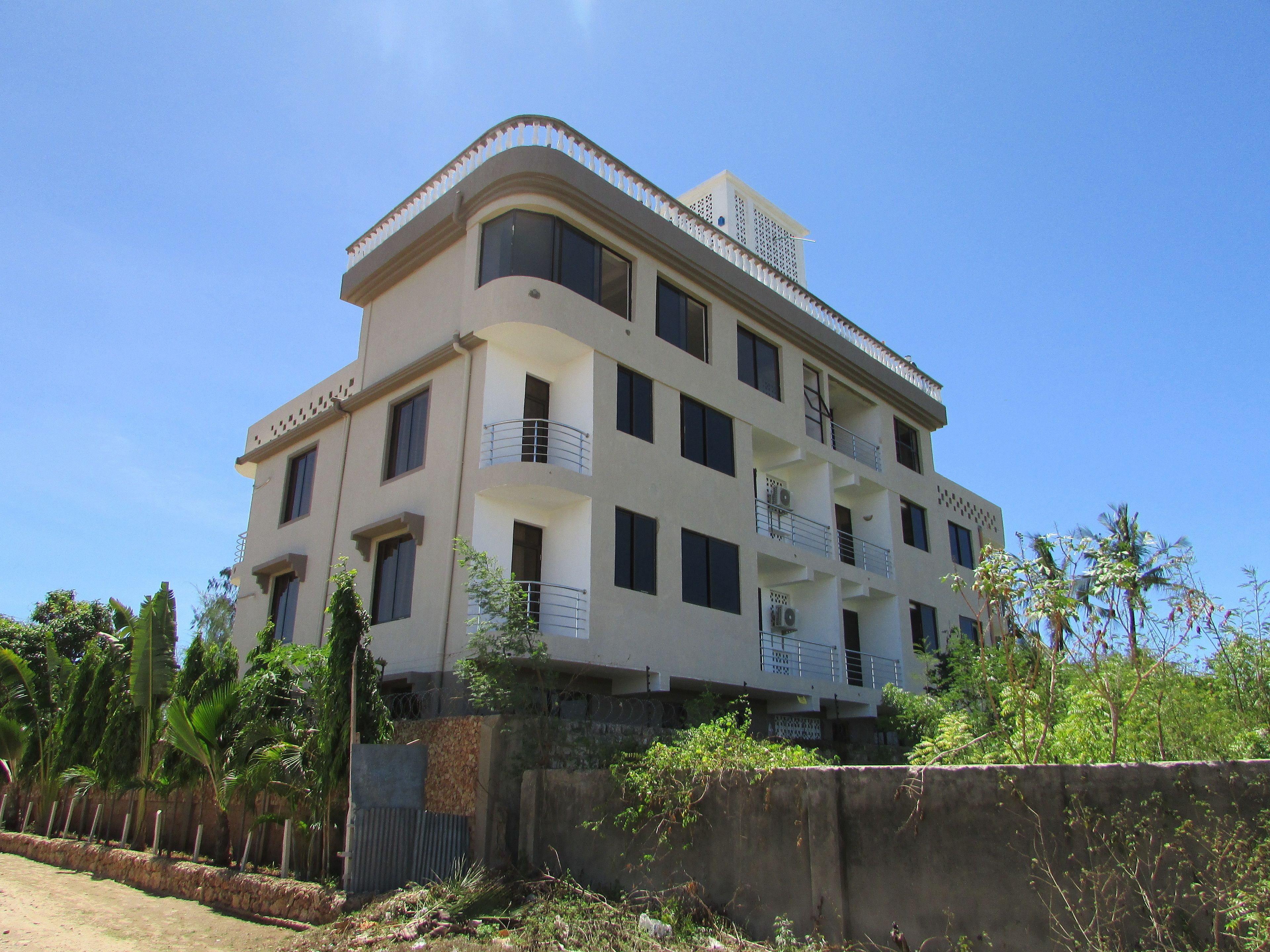 A multi-story building with balconies, a flat roof, and a concrete base.