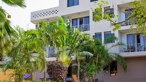 A multi-story building with balconies, surrounded by lush greenery including palm trees and other tropical plants.