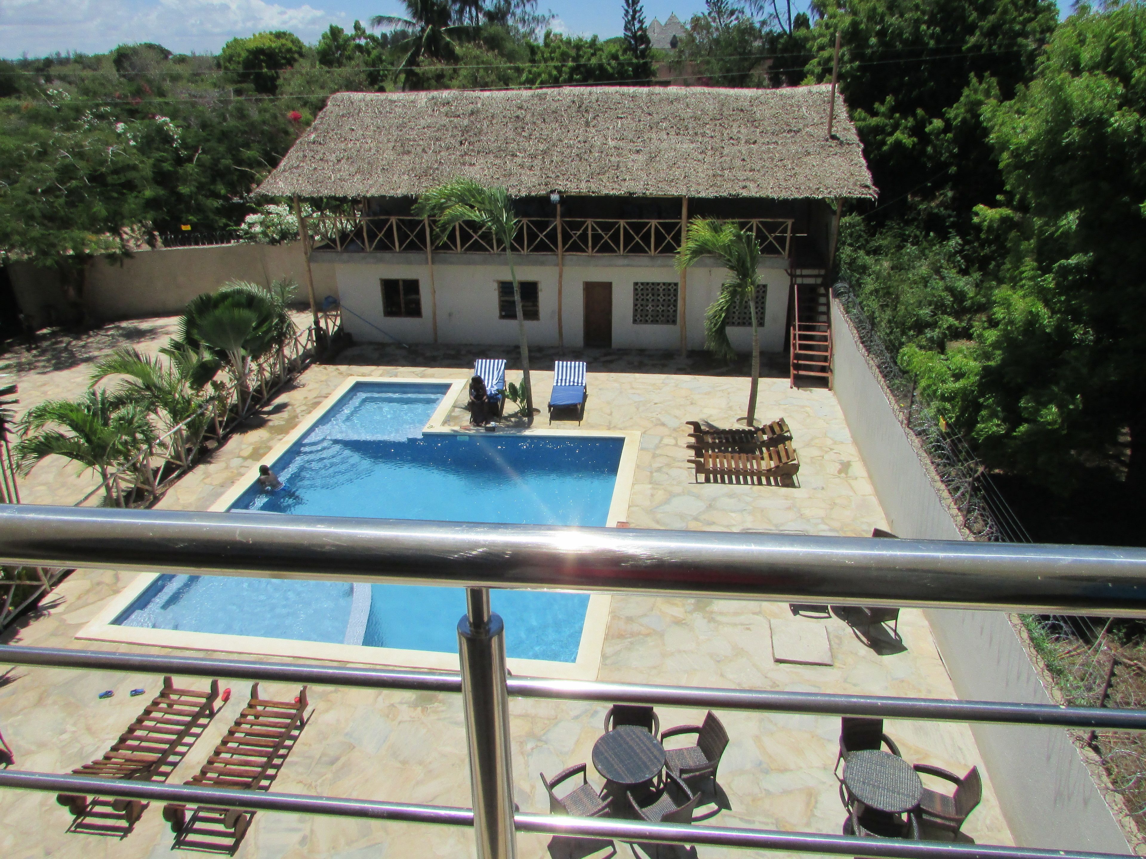 Un área de piscina con una pileta rectangular, sillas de descanso y una mesa de comedor con sillas.