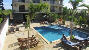 A hotel with a swimming pool, outdoor seating, and a multi-story building with balconies.
