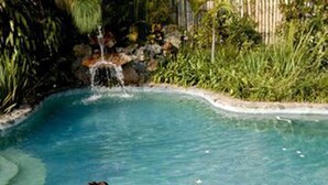 A woman relaxing in a hot tub surrounded by a stone border, with a waterfall and lush greenery in the background. - Hotel Valle Místico (Tepoztlán)