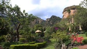 A lush garden with neatly trimmed hedges, a stone bench, and a rock formation. - Hotel Valle Místico (Tepoztlán)