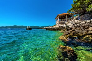 A coastal building with a stone facade and a tiled roof, situated on a rocky shoreline with clear blue water. - Villa Ragusea with Heating Pool and Private Beach (Slano)