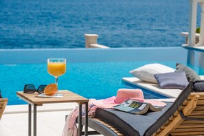 A poolside lounge with a glass of orange juice, sunglasses, and a book on a wooden table.