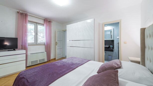 Un dormitorio con cama, televisor, cómoda y ventana con cortinas.