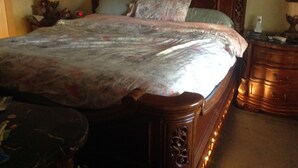 A wooden bed with a headboard, a bedside table with a lamp, and a nightstand with a clock. - 3 bedroom house w/private heated salt water pool, bbq, quiet location  (Pembroke Pines)