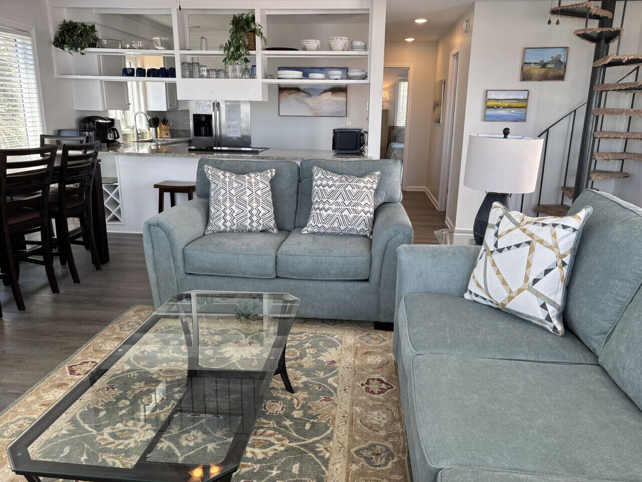 A living room with a grey sofa, a glass coffee table, and a patterned rug.