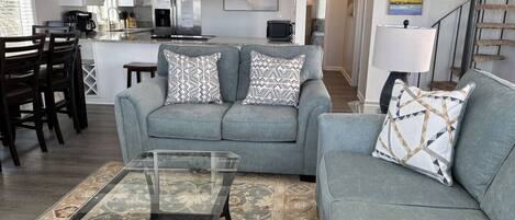 A living room with a grey sofa, a glass coffee table, and a patterned rug.