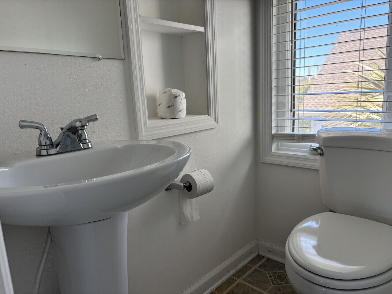 Un baño con lavamanos, inodoro y ventana con persianas.