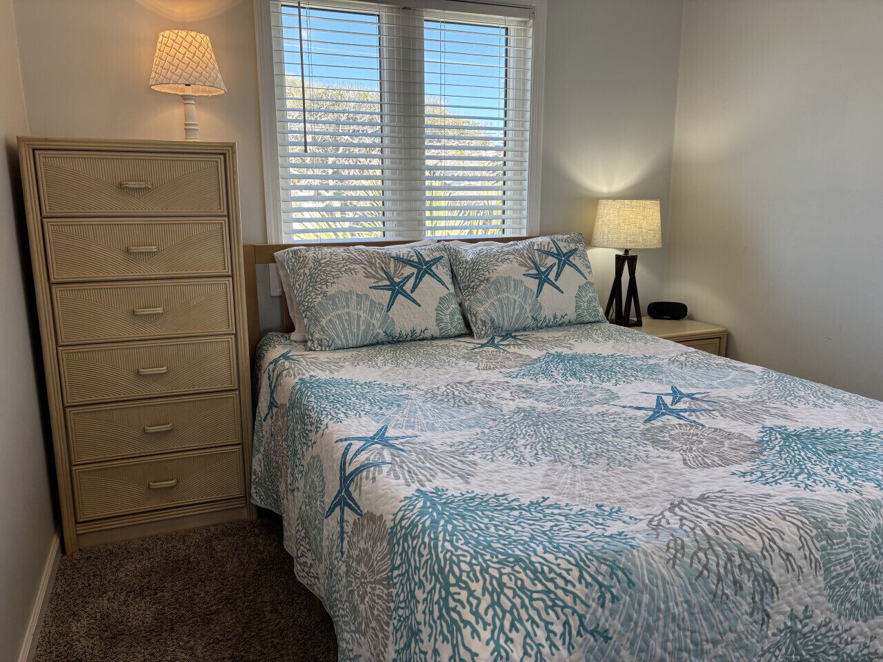 A bedroom with a bed, a nightstand, a dresser, and a window with blinds.