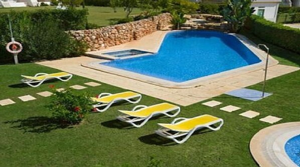 Una piscina con tres tumbonas, un muro de piedra y un césped bien cuidado.