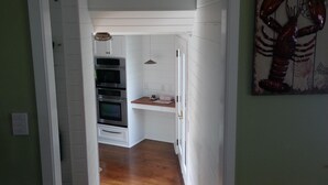 A hallway leading to a kitchen with white cabinetry, a lobster artwork on the wall, and a wooden floor. - Chatham Village - Center - Main Street Center Area (Chatham)