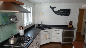 A kitchen with white cabinets, a black countertop, a stainless steel stove, and a whale watching trip sign on the wall. - Chatham Village - Center - Main Street Center Area (Chatham)