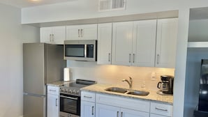 A modern kitchen with white cabinets, stainless steel appliances, a double sink, and a coffee maker. - NEW COMPLETE REMODEL, MELBOURNE HARBOUR VIEWS (Melbourne)