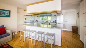 A modern kitchen with a central island, bar stools, and a dining area with a sofa.