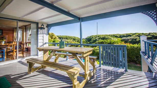 A covered outdoor deck with wooden picnic tables and benches, overlooking a lush green landscape.