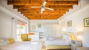 A hotel room with two beds, a ceiling fan, wooden beams, a small desk, and a chair.