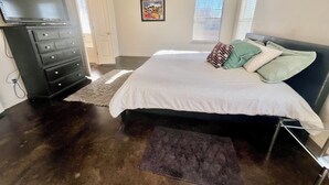 Ein Schlafzimmer mit Bett, Kommode, Fernseher und Kunstwerk an der Wand.