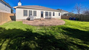 Ein eingeschossiges Haus mit Terrasse, Grill und einem umzäunten Garten.
