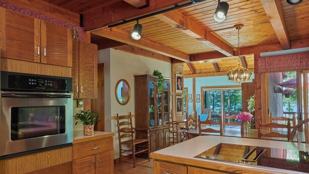 Una cocina con armarios de madera, un horno de acero inoxidable, un comedor con sillas de madera y un ventanal con vistas a zonas verdes.