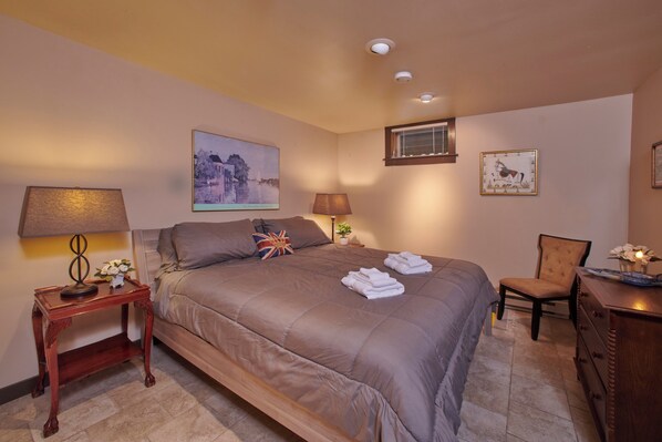 A neatly arranged hotel room with a large bed, a bedside table with a lamp, a chair, and a dresser.