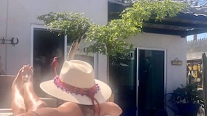 Una persona descansando en un banco exterior blanco, con un edificio y un letrero que dice "DRINK" al fondo.