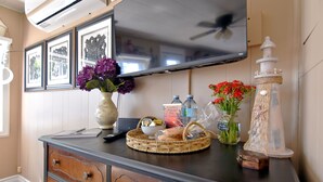 Un téléviseur à écran plat fixé au-dessus d’une commode en bois dotée de tiroirs, un panier en osier et des objets décoratifs, notamment des vases avec des fleurs.
