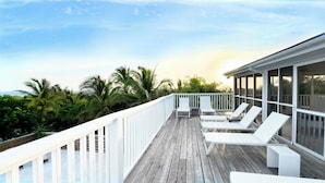 Een houten terras met witte leuningen en loungestoelen.