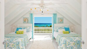 Een slaapkamer met twee bedden, uitzicht op de oceaan en een plafondventilator.
