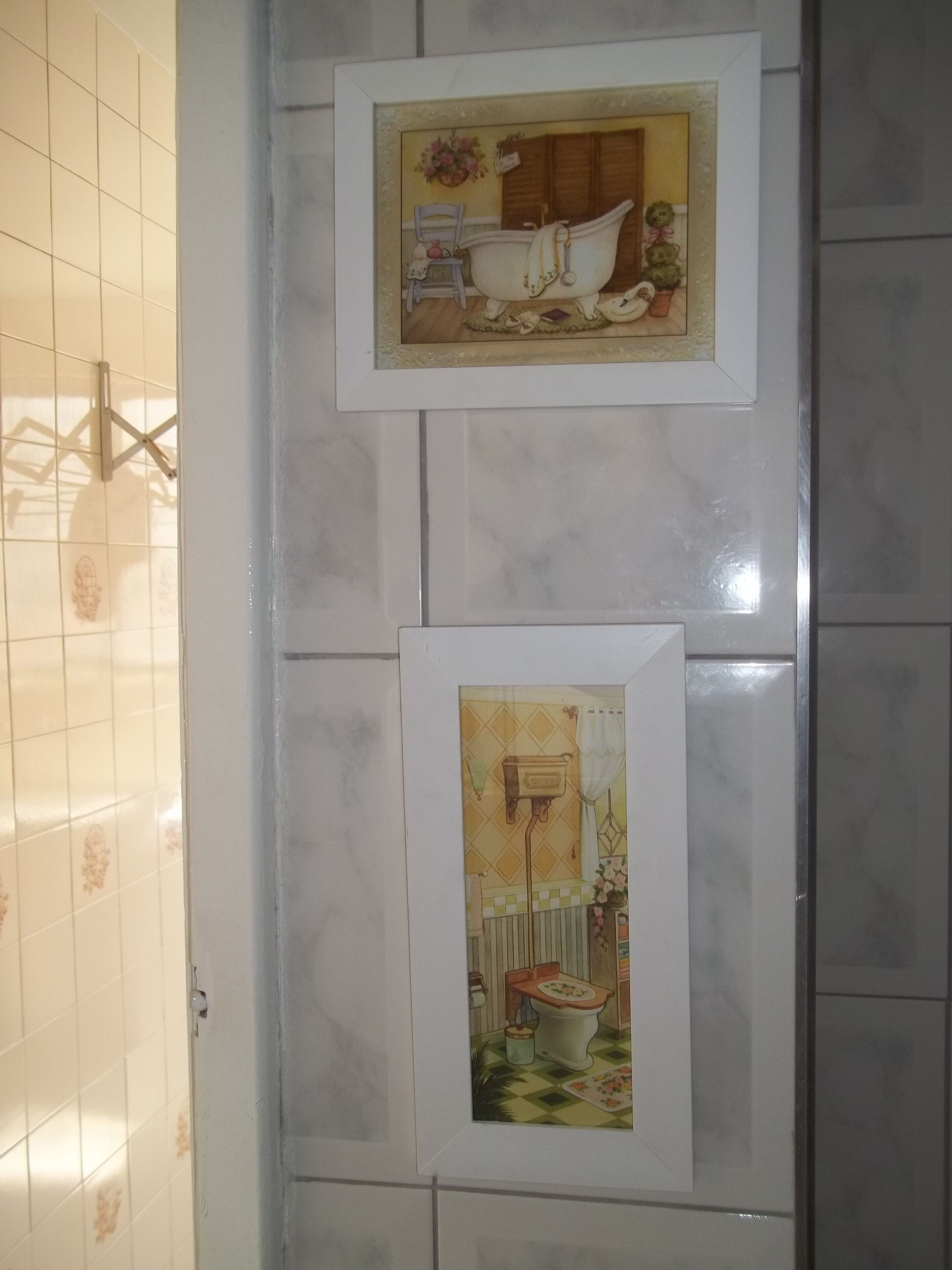 Twee ingelijste foto’s van klassieke badkamerinterieurs op een betegelde muur.