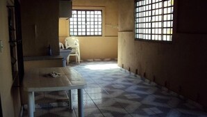 Ein Zimmer mit Fliesenboden, einem Tisch und zwei vergitterten Fenstern.