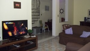 Ein Wohnzimmer mit Fernseher auf Holzständer, einem braunen Sofa und einem gemusterten Boden.