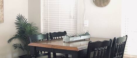 A dining area with a wooden table and four chairs, a potted plant, and a wall-mounted sign with the word "gather".