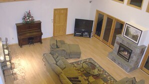 Un salon spacieux avec un grand canapé d’angle, une cheminée, un téléviseur et un piano.