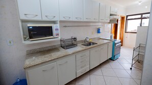 Uma cozinha com armários brancos, micro-ondas, pia e fogão.
