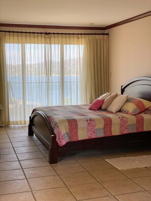 A bedroom with a bed, a view of the sea through sheer curtains, and a tiled floor. - Spectacular Condominio View of Flamingo Beach and Potrero Bay   (Playa Flamingo)