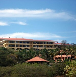 A multi-story hotel with a red roof, surrounded by greenery and palm trees. - Spectacular Condominio View of Flamingo Beach and Potrero Bay   (Playa Flamingo)