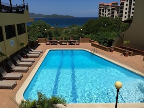 A rectangular swimming pool with clear blue water, surrounded by lounge chairs and a view of the ocean. - Spectacular Condominio View of Flamingo Beach and Potrero Bay   (Playa Flamingo)