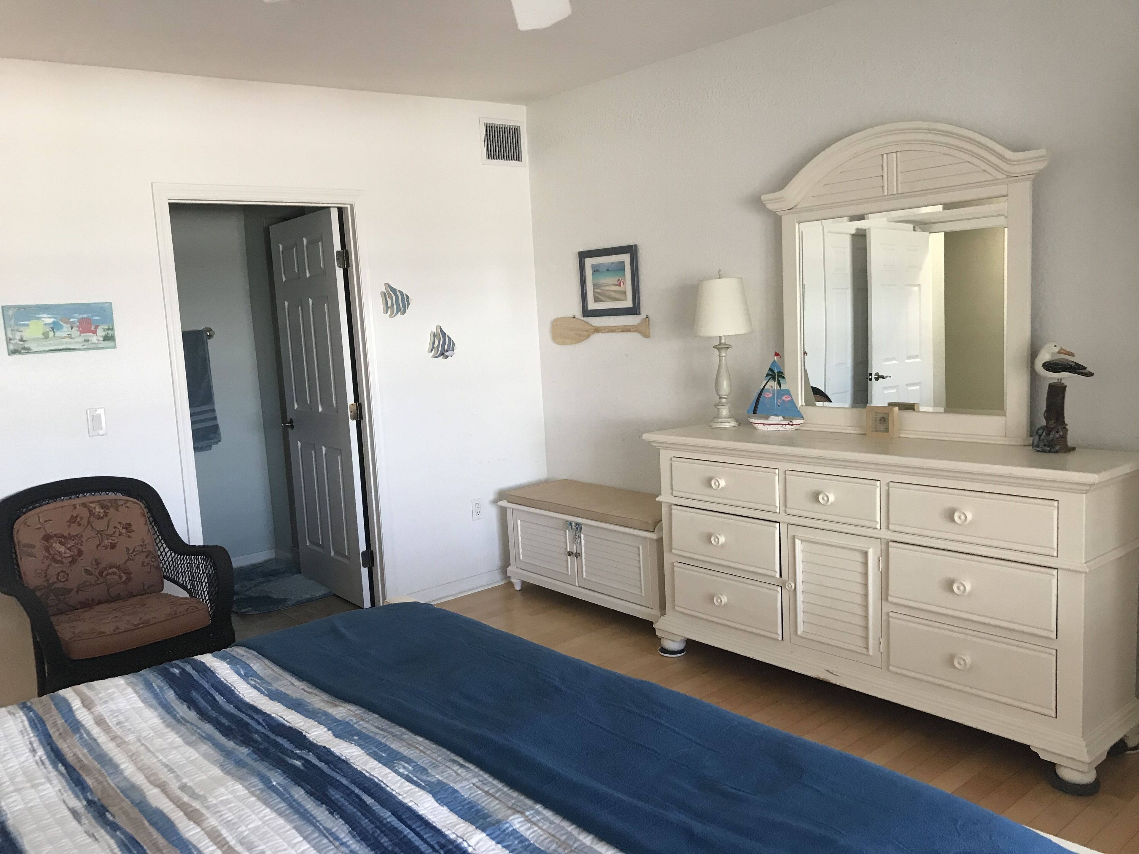 Ein Schlafzimmer mit Bett, Kommode, Stuhl und einer Tür zu einem anderen Raum.