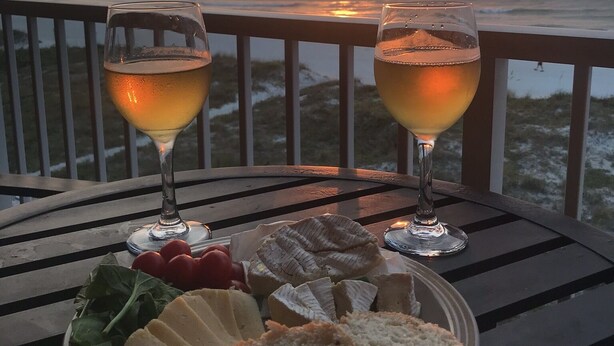 Ein Tisch mit zwei Weingläsern, Käse und Brot sowie Blick auf den Sonnenuntergang über dem Meer.